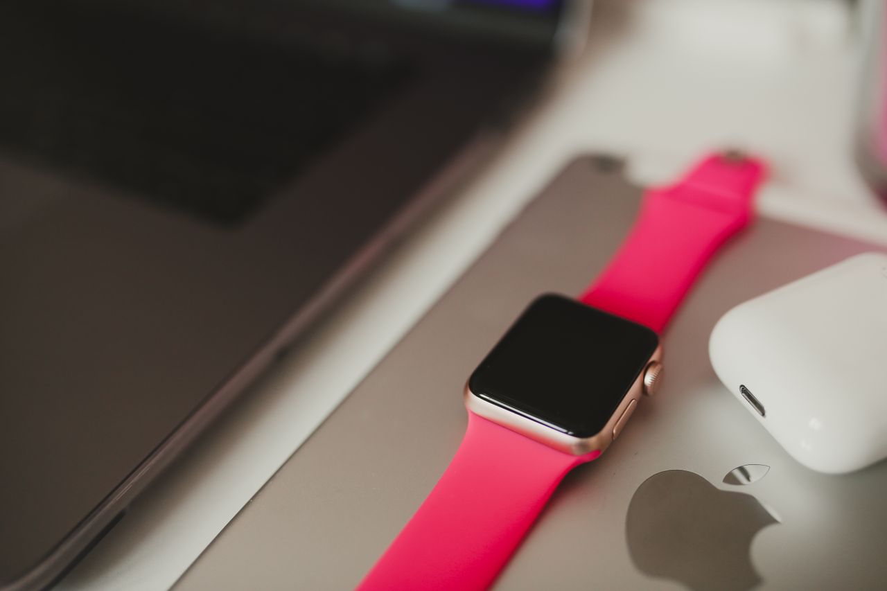 social-feed-img-05 A stylish smartwatch with a pink band placed on a laptop surface, surrounded by modern gadgets.