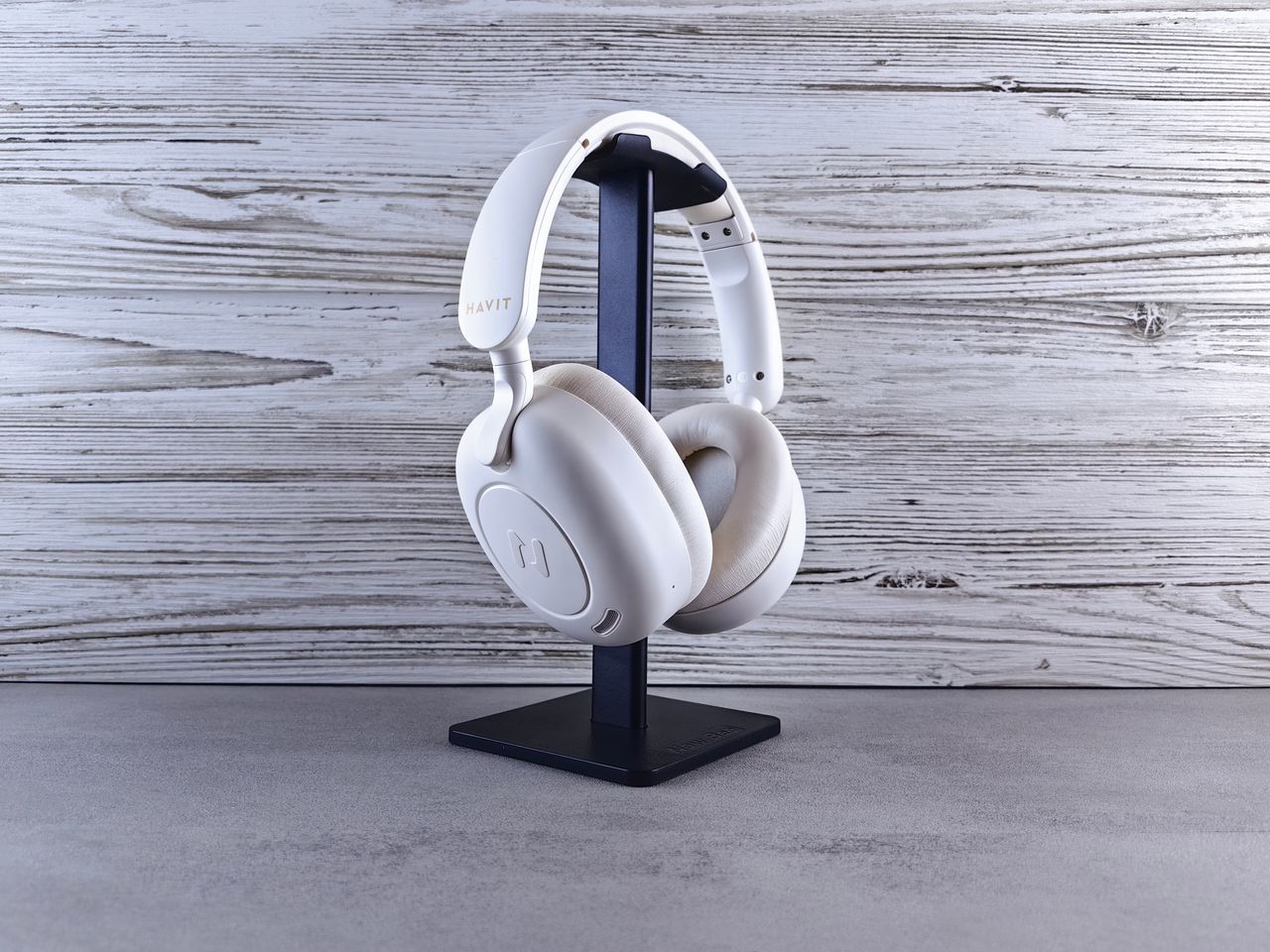 Minimalist photo of white wireless headphones on a stand against wood background.