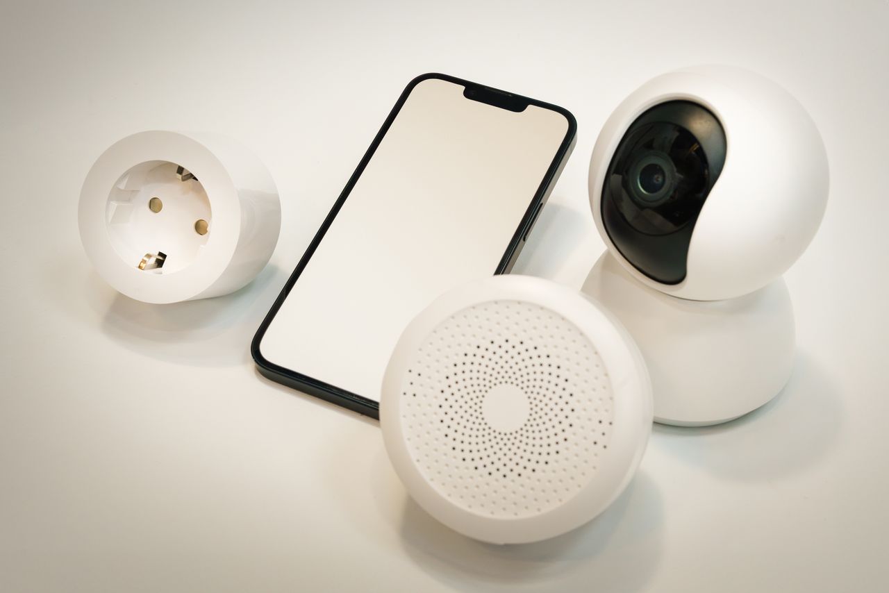 quality-assurance-02 Smart home gadgets including a security camera, speaker, and smartphone displayed on a white surface.